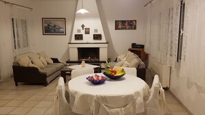 A cozy living room with a fireplace, a dining table with a fruit bowl, and a sofa. - Silver Villa Raches, Sky Maisonette, 2 Floor Villa (Raches)
