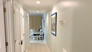 Un couloir doté d’un sol carrelé, de portes blanches, d’un coin repas avec une table et des chaises, et d’un tableau encadré accroché au mur.