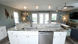 Una cocina amplia con una isla central, muebles blancos, electrodomésticos de acero inoxidable e iluminación colgante.