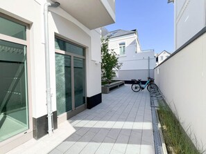 Um corredor exterior estreito com chão em mosaico, uma bicicleta e um vaso com uma árvore.