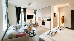 A modern hotel room with a sofa, a bed, a small dining table, and a kitchenette. - Anchorage - Enjoy your vacation close to the beach and the city center (Sylt)