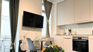 A modern kitchen with a flat-screen TV, a dining table with chairs, and a vase of flowers. - Anchorage - Enjoy your vacation close to the beach and the city center (Sylt)
