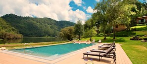 Un área de piscina con sillones de descanso, piscina y vistas a un lago y montañas.