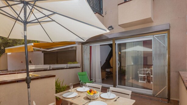 Une terrasse avec une table dressée pour deux personnes, une chaise verte et un grand parasol.