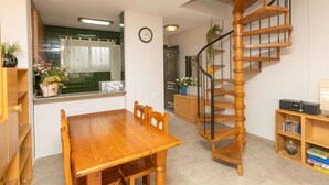 Un espace de vie compact comprenant une table à manger en bois, des chaises, un escalier en colimaçon et un petit coin cuisine avec une fenêtre.