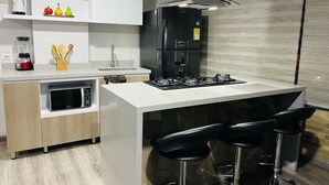 A modern kitchen with a central island, bar stools, a built-in oven, and a coffee machine. - 502 Hermoso Apartamento Amoblado Movistar Arena (Bogotá)