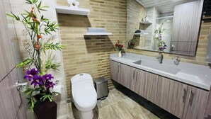 A modern bathroom with a toilet, sink, and mirror. There are plants and flowers on the counter. - 502 Hermoso Apartamento Amoblado Movistar Arena (Bogotá)