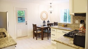 A kitchen with granite countertops, a dining table with chairs, a stove, and a window with blinds. - Mile to Ocean! Fully Fenced Private SoCal Cottage (Oceanside)