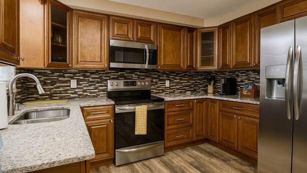 A kitchen with wooden cabinets, a stainless steel refrigerator, a microwave, and an oven. - Remodeled 2BR Near Gulf Beaches Fast Wi-Fi (Holiday)