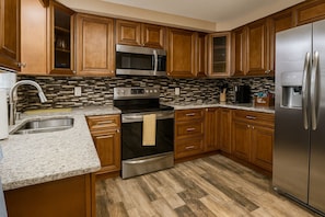 A kitchen with wooden cabinets, a stainless steel refrigerator, a microwave, and an oven.