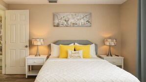 A bedroom with a bed, two bedside tables, a nightstand, a door, and a wall-mounted artwork. - Remodeled 2BR Near Gulf Beaches Fast Wi-Fi (Holiday)