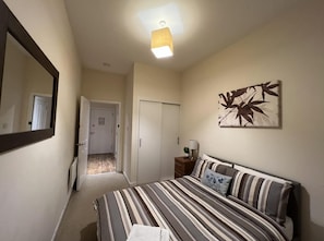 A bedroom with a bed, a nightstand, a lamp, a mirror, and a door leading to another room. - Aberdeen Stay Central 2-bedrooms Apt-no Party (Aberdeen)