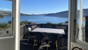 A patio with a table and chairs, overlooking a lake and hills. - Amazing views! 5 mins to beach (Dunedin)