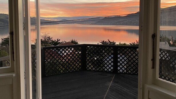 An open door leading to a balcony with a view of a lake and mountains during sunset. - Amazing views! 5 mins to beach (Dunedin)