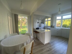 A modern kitchen with white cabinetry, a central island, and a dining area with a round table and chairs. - Amazing views! 5 mins to beach (Dunedin)