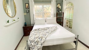 Un dormitorio con cama, mesita de noche, cómoda, ventana con cortinas, espejo y aire acondicionado de pared.