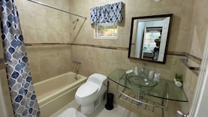 Un baño con bañera, inodoro y lavamanos de vidrio.