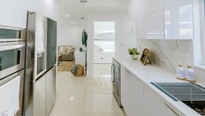 A modern kitchen with stainless steel appliances, a marble countertop, and a view to a living area. - Encanto Family, cozy patio & pool, near to everything (Miami)