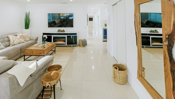 A modern living room with a sofa, coffee table, and fireplace. There is a large mirror and a plant on the wall. - Encanto Family, cozy patio & pool, near to everything (Miami)