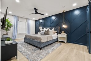 A modern bedroom with a bed, bedside tables, a ceiling fan, and a large window with curtains. - New Modern Ranch Home in Quiet Neighborhood of ATL (Atlanta)