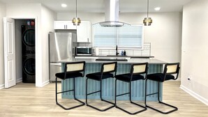 A modern kitchen with a central island, bar stools, a built-in oven, and a stainless steel refrigerator.
