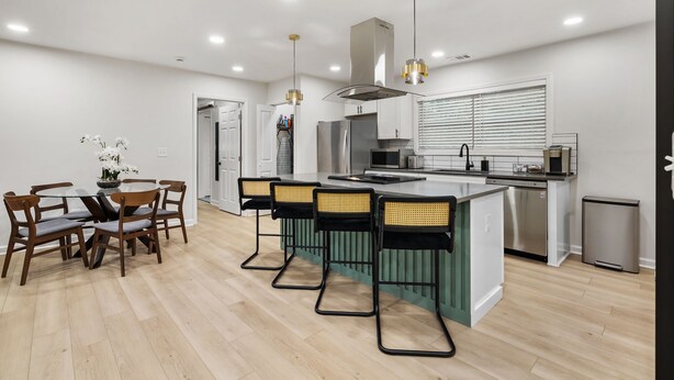 A modern kitchen with a central island, bar stools, and a dining table with chairs.