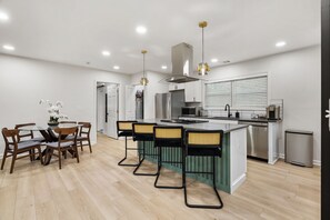A modern kitchen with a central island, bar stools, and a dining table with chairs. - New Modern Ranch Home in Quiet Neighborhood of ATL (Atlanta)