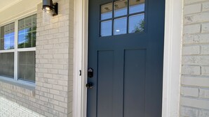 A dark blue front door with a window above it, a light fixture on the wall, and a doormat at the entrance.