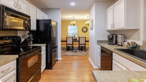 A kitchen with white cabinets, a black refrigerator, a microwave, and a stove. There is a dining area with a table and chairs in the background.