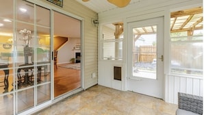 A covered patio area with a sliding glass door leading to an interior space, a wooden ceiling, and a view of a backyard.