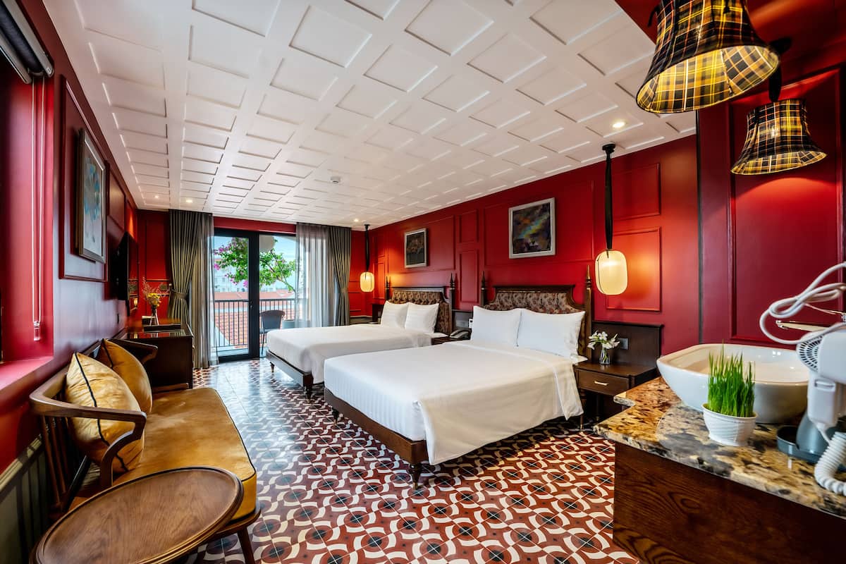 Habitación de hotel con dos camas, zona de estar, baño con lavamanos grande y vistas al exterior.