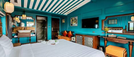 A hotel room with a large bed, a wooden desk, a bathroom with a sink and mirror, and teal walls.