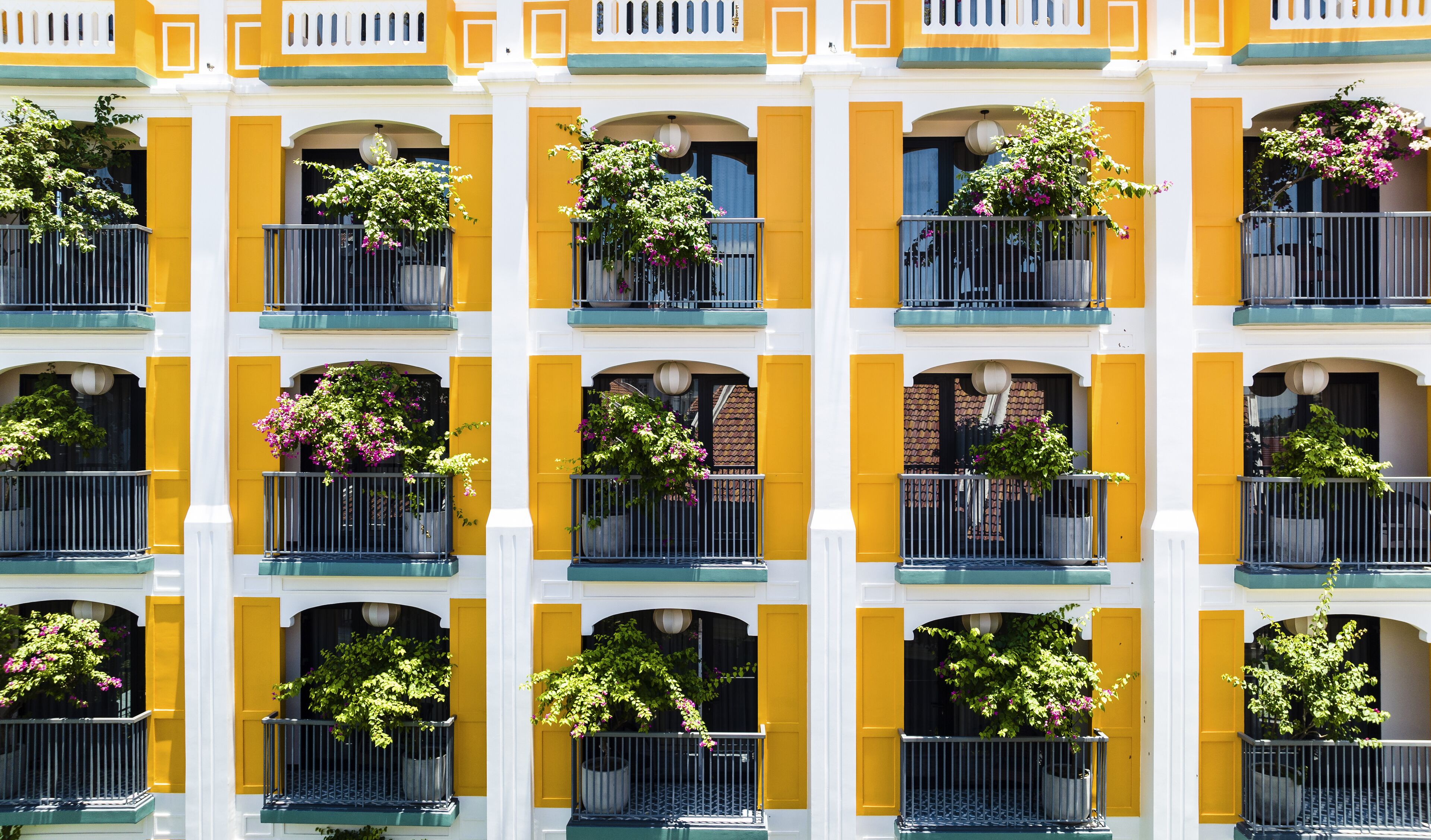Une façade d’immeuble ornée de nombreux balcons, chacun étant doté d’une rambarde et de plantes en pot.