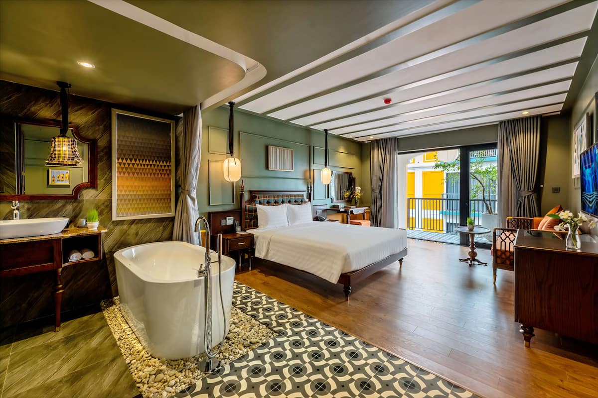 Habitación de hotel con una cama grande, una bañera, un tocador con espejo y vistas al exterior.