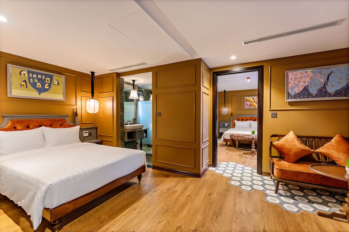 Habitación de hotel con una cama grande, un sofá, un escritorio y un baño visible a través de una puerta abierta.