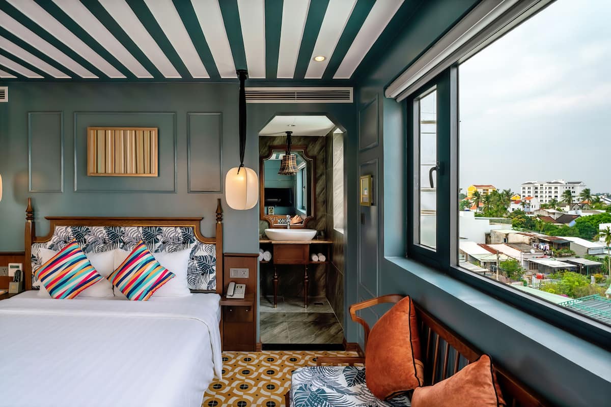 Un dormitorio con una cama grande, vistas de la ciudad y un baño con lavabo y espejo.