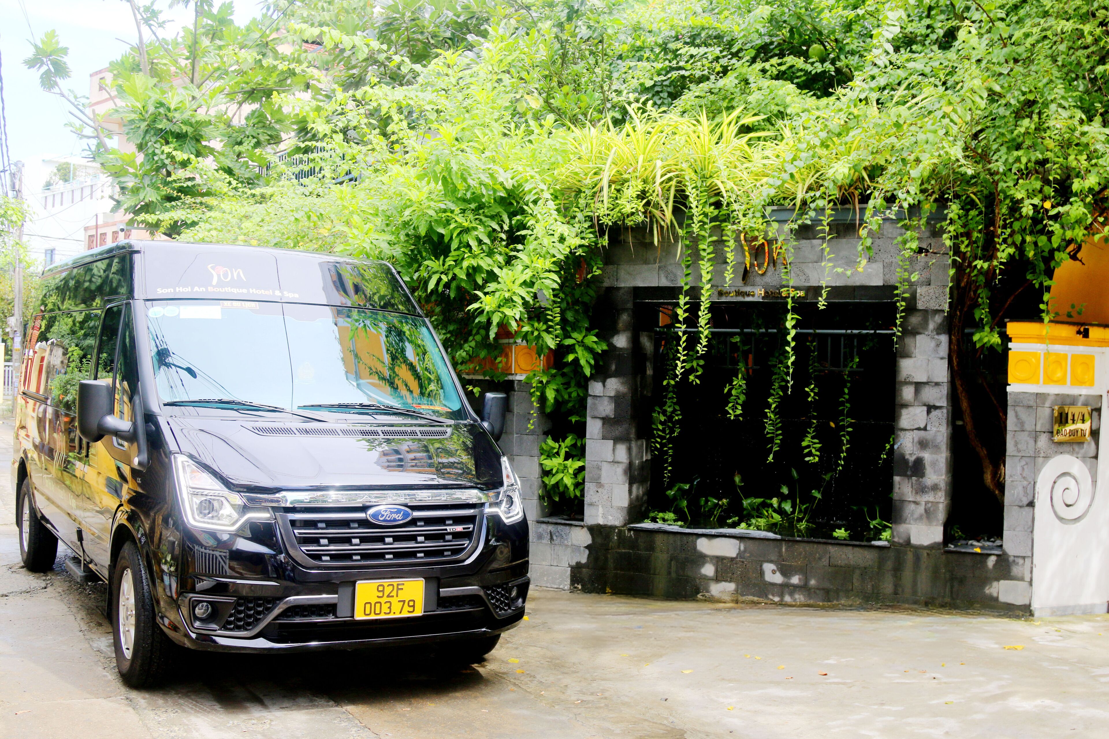 A black Ford van parked in front of a building with a stone facade and greenery.