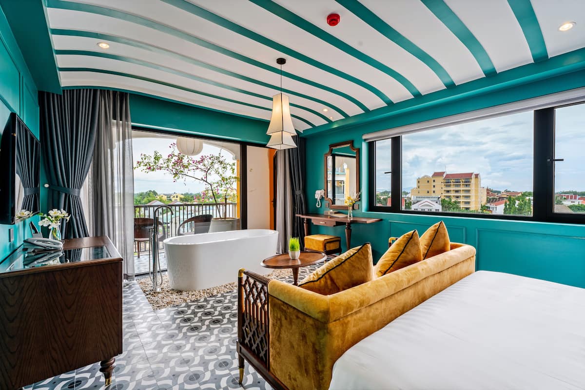 Habitación de hotel moderna con una cama grande, una bañera, un tocador y un balcón con vistas a la ciudad.