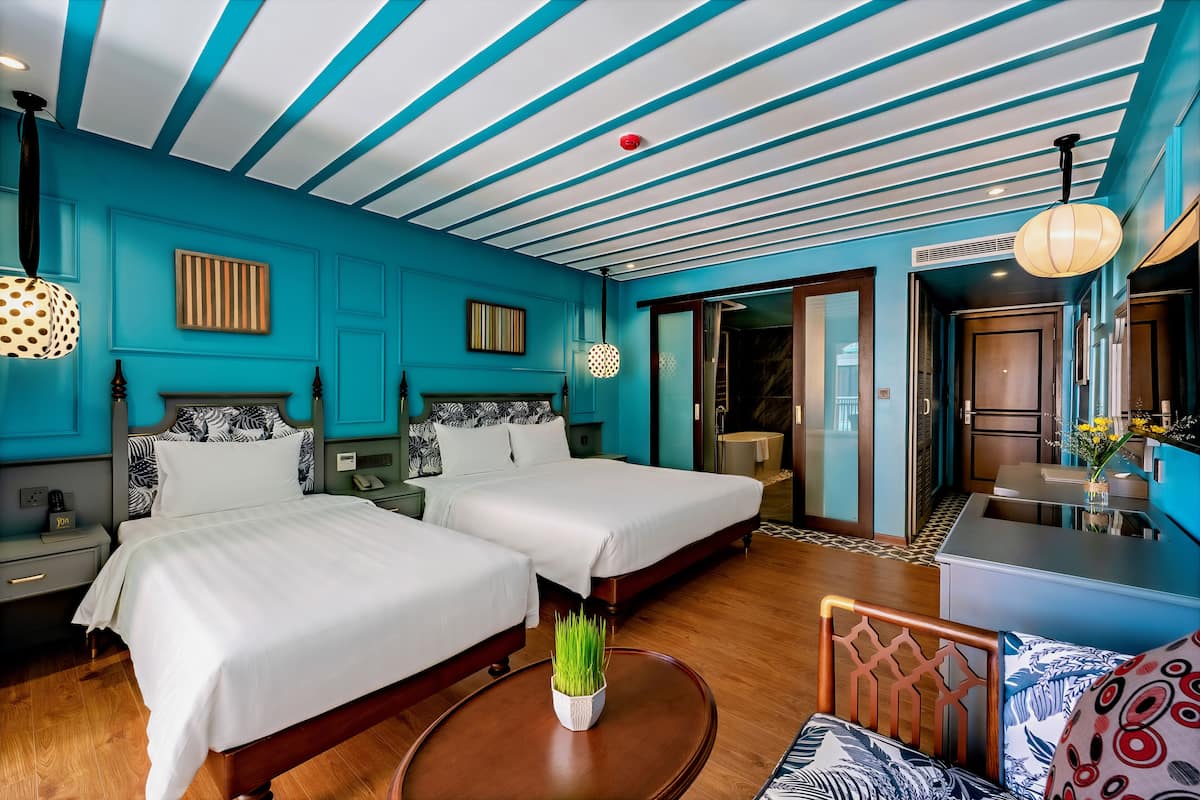 Habitación de hotel con dos camas, zona de comedor y baño.