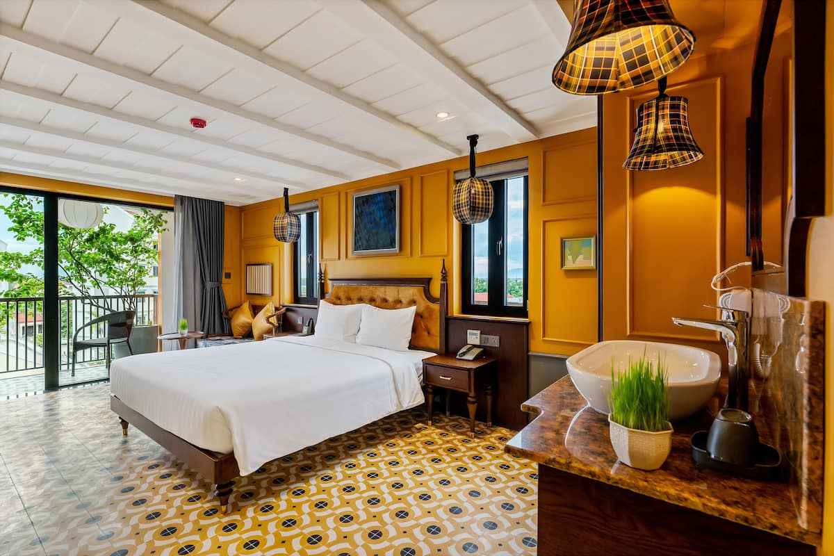 Habitación de hotel con una cama grande, una mesita de noche, un baño con lavamanos amplio y un balcón con vista a zonas verdes.