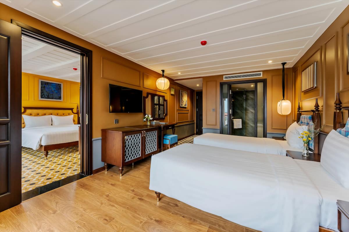 Habitación de hotel con dos camas, piso de madera, televisor y espejo.