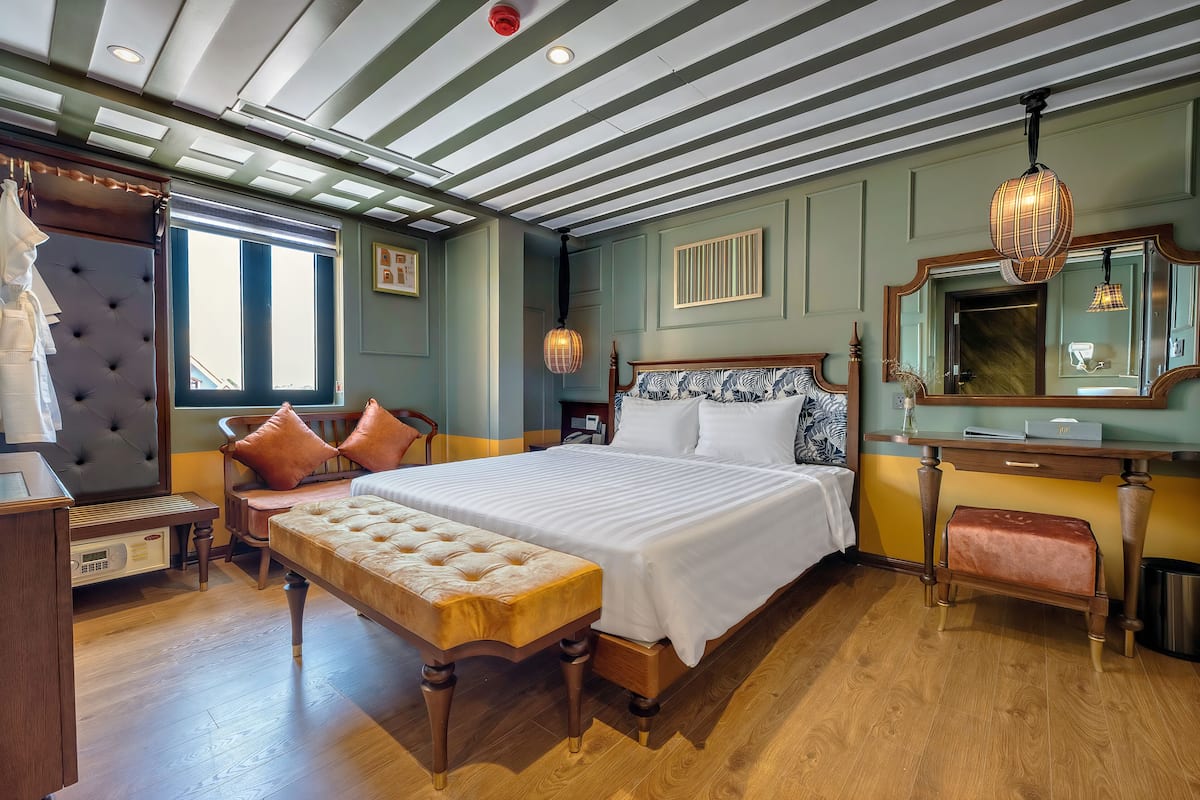 Un dormitorio con una cama grande, un banco de madera, una mesita de noche, un aparador y un espejo.