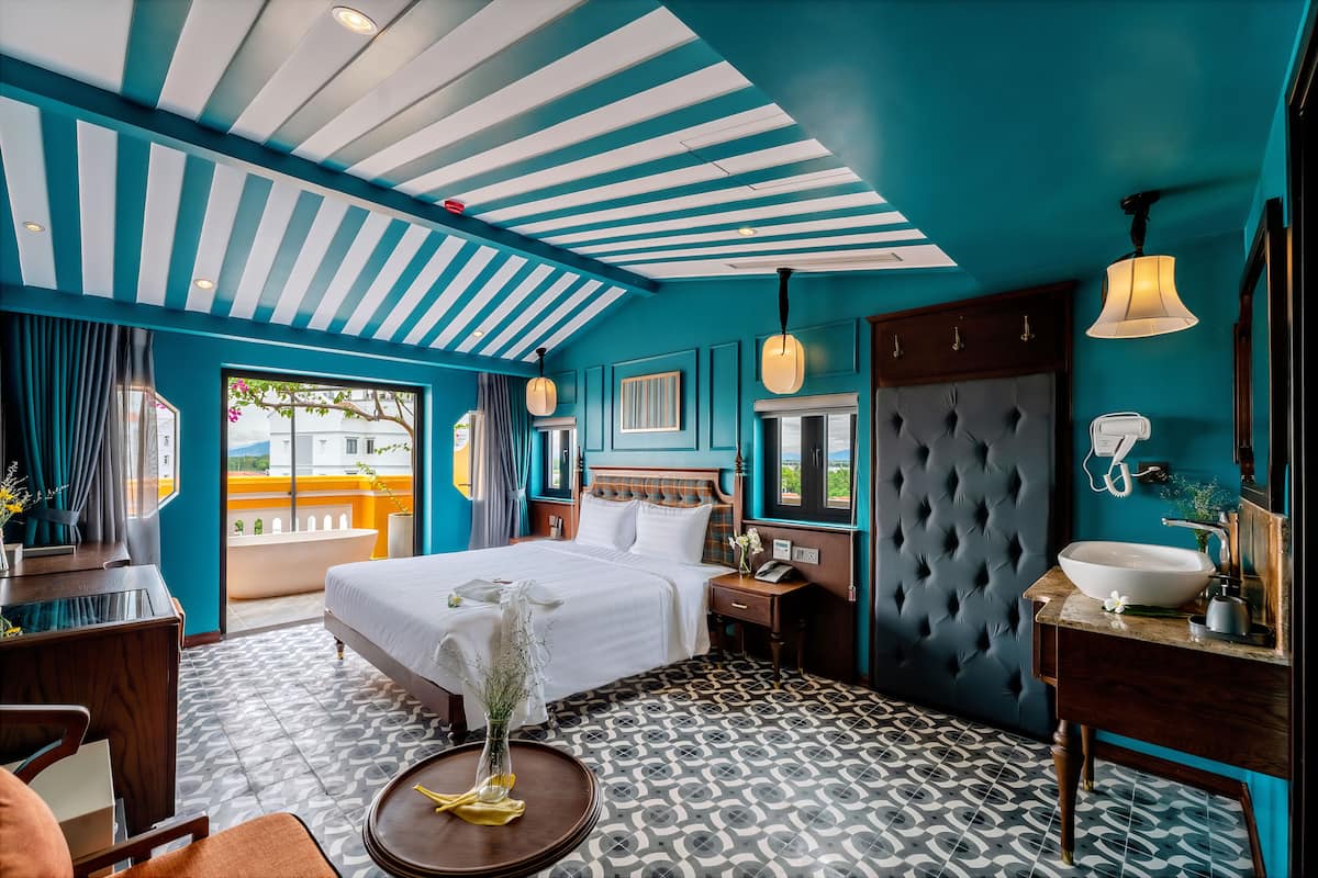 Habitación de hotel con una cama grande, tocador con lavamanos, ventana con cortinas y piso estampado.