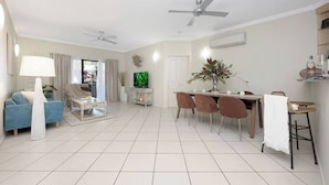 Un salon spacieux comprenant un canapé, une table basse, un téléviseur, une table à manger avec des chaises et un ventilateur de plafond.