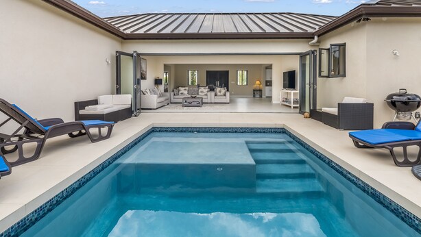 Una piscina con lettini, un'area patio e vista sul soggiorno.