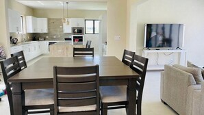 Una cucina moderna con mobili bianchi, un'isola centrale e una zona pranzo con tavolo e sedie in legno.