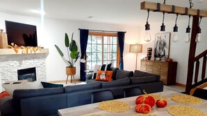 Ein modernes Wohnzimmer mit einem dunkelgrauen Ecksofa, einem Holzesstisch mit gewebten Tischsets und einem Kamin.