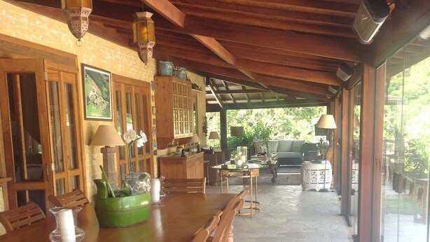 A spacious covered patio with a wooden dining table and chairs, stone flooring, and a view of greenery outside. - Country House (Amparo)