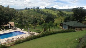 A pool area with a grassy lawn, a small building, and hills in the background. - Country House (Amparo)