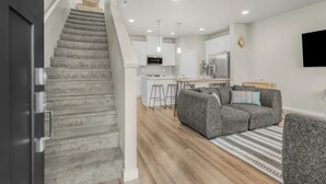 A modern kitchen with white cabinets, a central island, and a dining area with a grey sofa and patterned rug. - Tranquil Townhome in Prime Location (Vancouver)